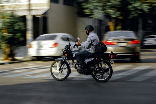 Free A motorcyclist wearing a helmet rides through city traffic on a bright day. Stock Photo