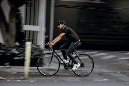 Free A man in casual attire riding a bicycle swiftly on a city street. Stock Photo