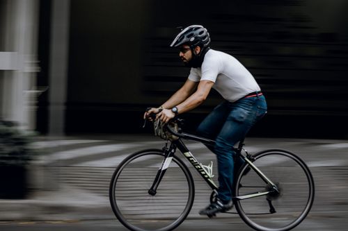Free A man in casual attire riding a bicycle swiftly through a city street, showcasing motion and focus. Stock Photo