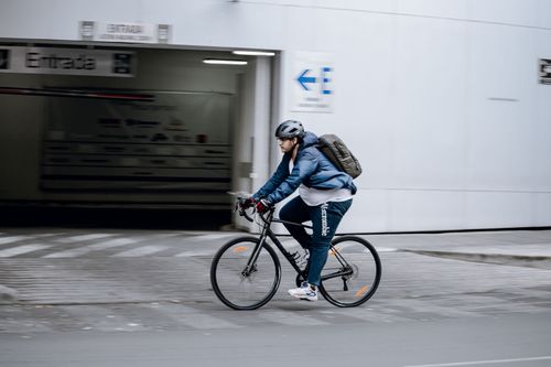 Free A man in a blue jacket cycling on an urban sidewalk with a backpack. Stock Photo