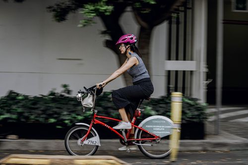 Free Active woman rides red bike outdoors during day, showcasing motion in urban environment. Stock Photo
