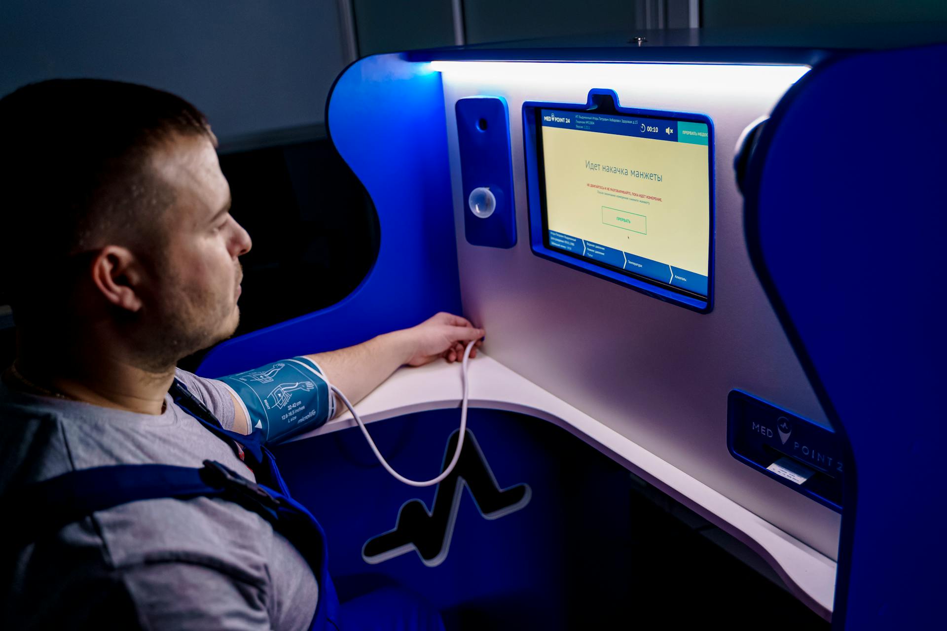 Man measuring blood pressure with a digital monitor at a self-service kiosk for telemedicine.