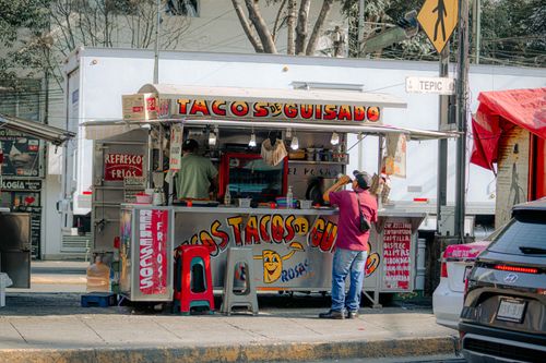 Free A bustling street vendor selling tacos in a colorful open-air stall on a sunny day. Stock Photo
