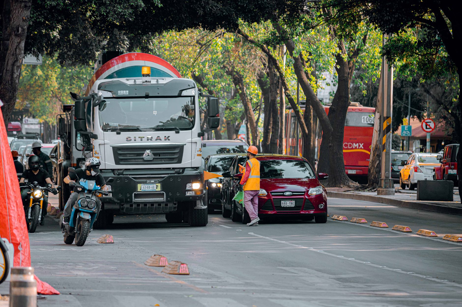 Street view of urban traffic with vehicles, motorbikes, and a worker in a city.