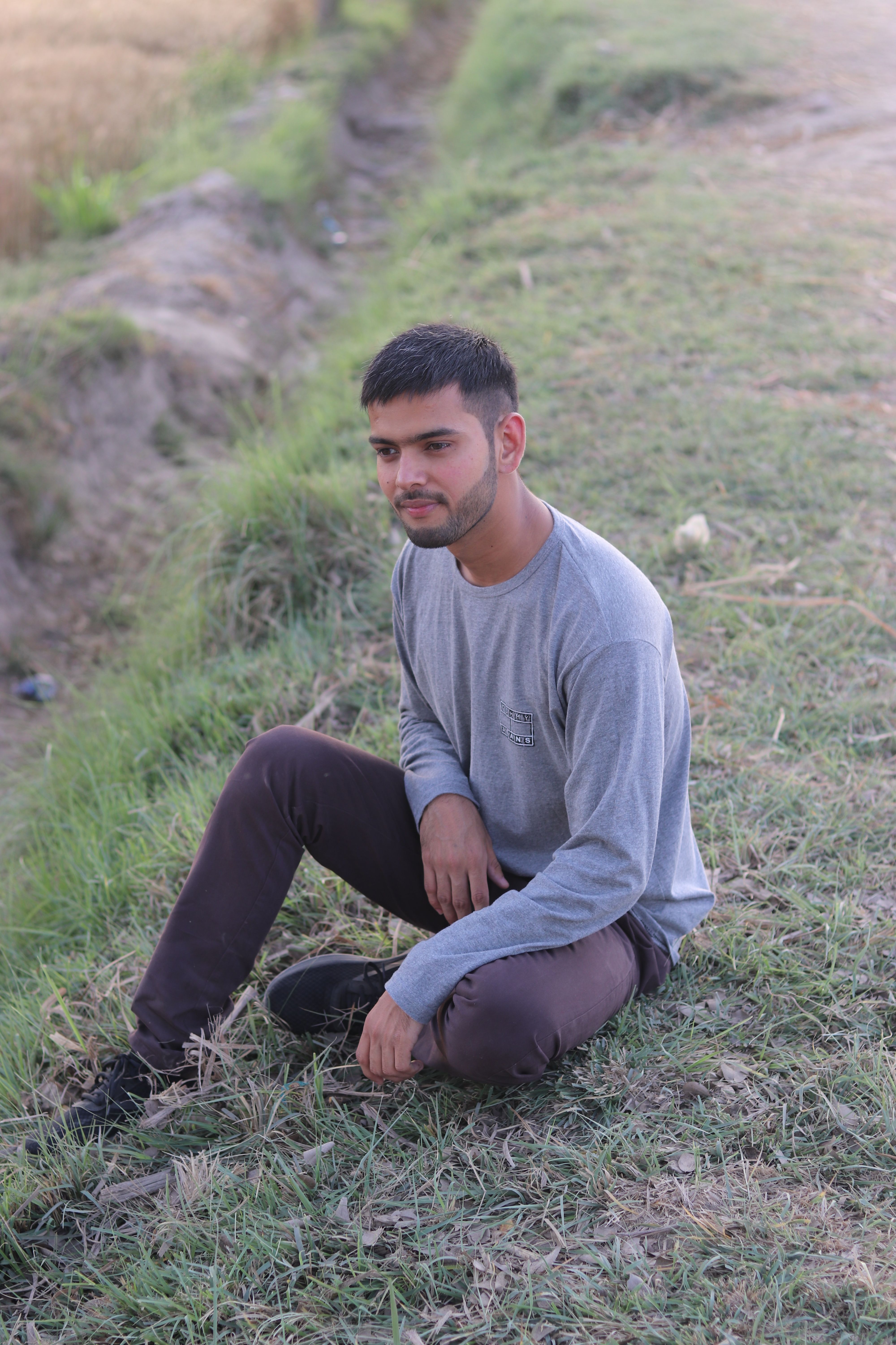A young man sitting thoughtfully on a grassy field, enjoying the outdoors.
