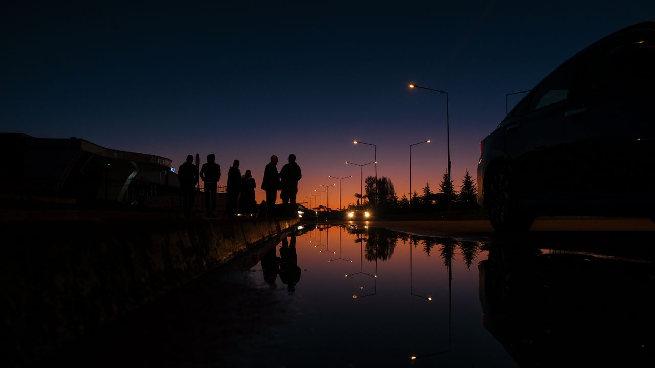 silhouettes of people against a twilight sky with streetlight reflecti