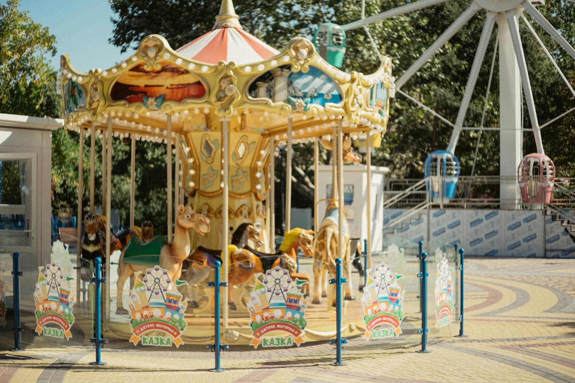 Colorful carousel at an outdoor amusement park, featuring animal rides in a summer setting.