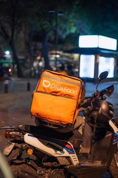 A food delivery scooter with an orange thermal bag parked at night in Ciudad de México.
