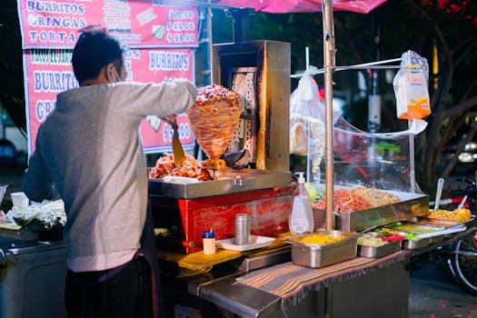 Street vendor in Mexico City cooking tacos al pastor on a busy night market stand.