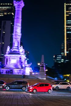 Illuminated Angel of Independence in CDMX with cars passing by, capturing a vibrant nighttime scene.