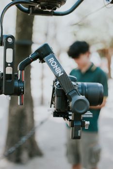 DSLR camera mounted on Ronin gimbal outdoors with blurred photographer in background.