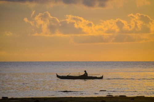 Free A fisherman in a boat silhouetted against a vibrant sunset sky over the calm sea. Stock Photo