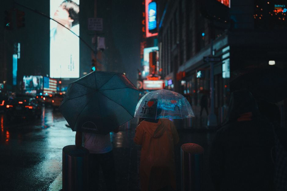 Vibrant Times Square at night with people holding umbrellas on a rainy street.