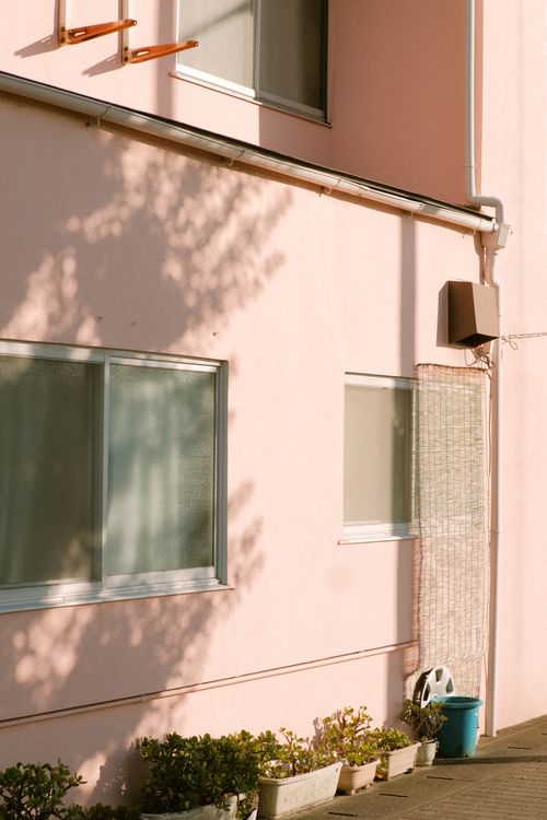 Free Soft pink wall of a residential building with windows and shadow play, capturing urban tranquility. Stock Photo