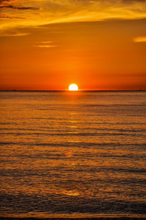 Free Stunning sunset over calm ocean waters with vivid orange and yellow hues. Stock Photo