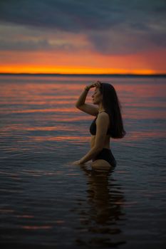 Peaceful scene of a woman standing in the ocean at sunset, showcasing tranquility and beauty.