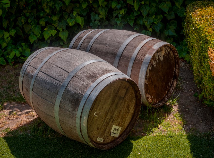 Regentonne aus Anthrazit an einem Fallrohr im Garten, auf stabilen Platten aufgestellt