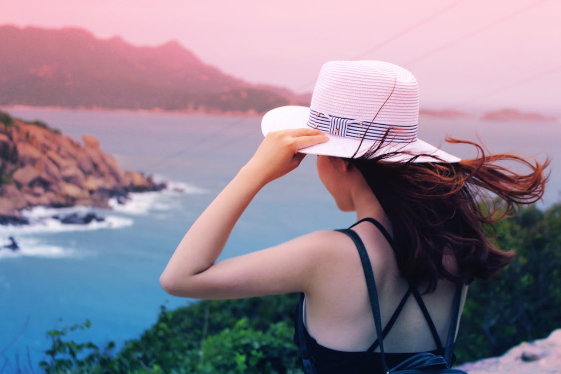 Gratis Wman Holding Wricker Shade Hat On Ocean View Foto a disposizione