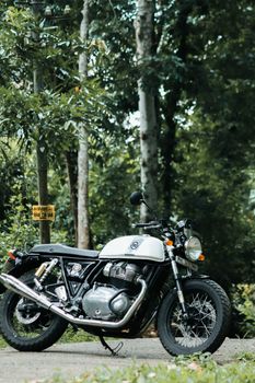 A white classic motorcycle parked on a forest road surrounded by lush greenery.
