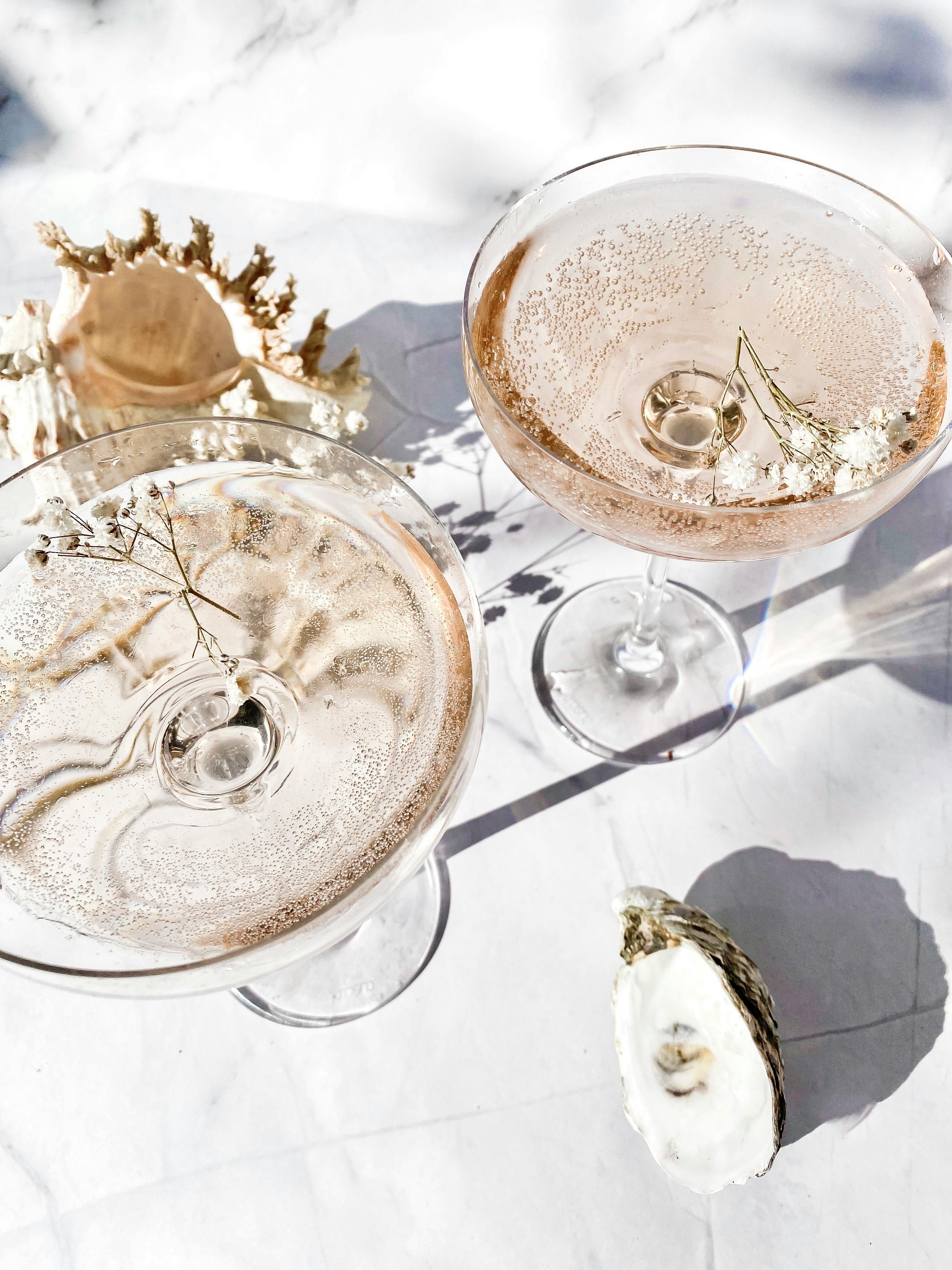 Two glasses of rose champagne with floral accents and an oyster, perfect for celebrations.