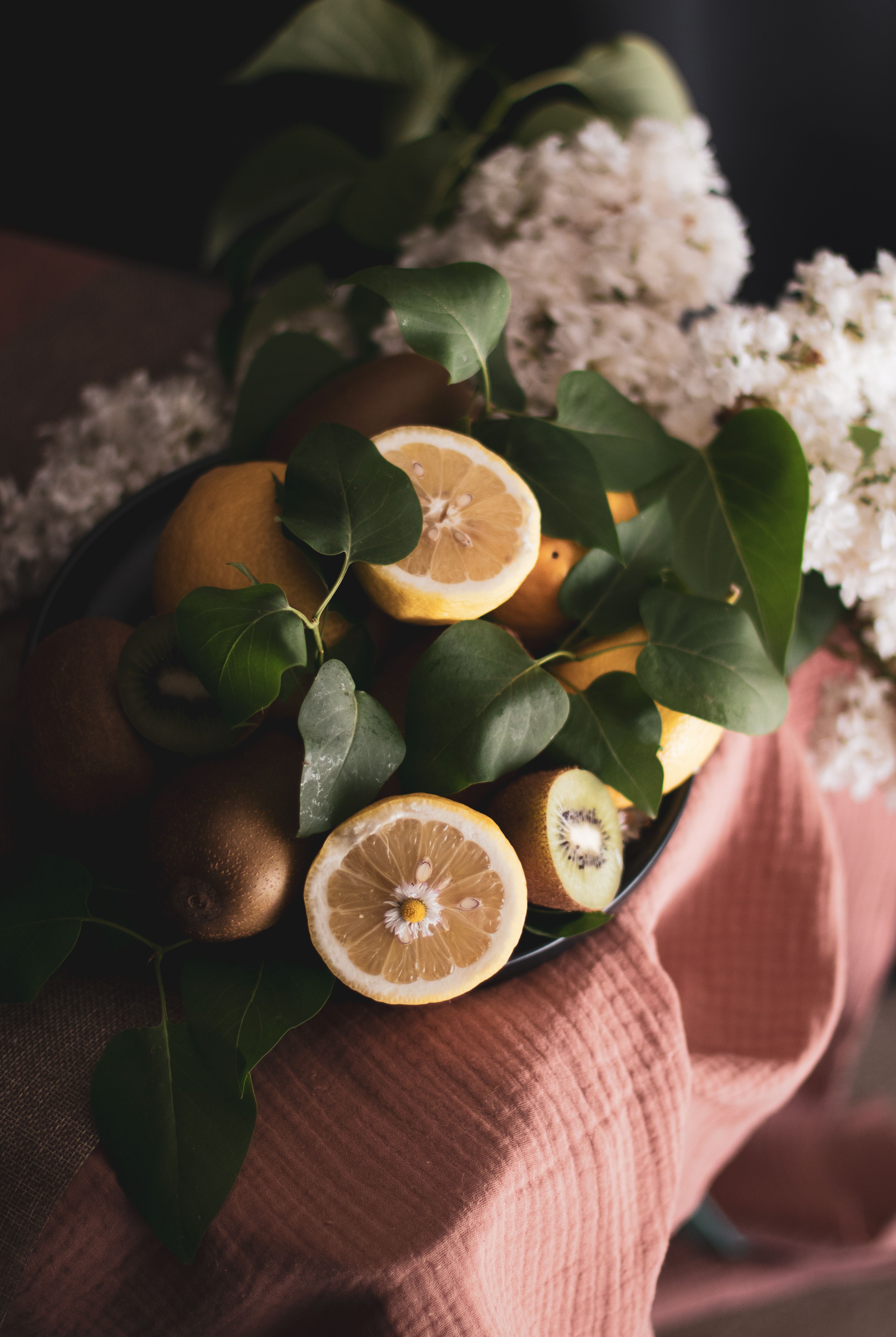 Artistic composition of sliced lemons, kiwis, and white lilac on a textured cloth.