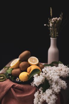 Artistic still life featuring lemons, kiwi, and flowers arranged beautifully against a dark background.