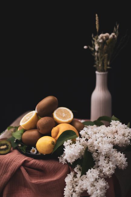 Artistic still life featuring lemons, kiwi, and flowers arranged beautifully against a dark background.