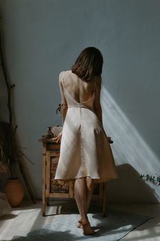 Elegant woman in a minimalist room with natural lighting and a simple open back dress.