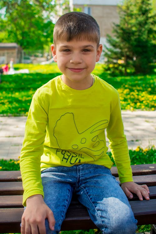 A Smiling Boy in Green Long Sleeves Sitting on a Wooden Bench 