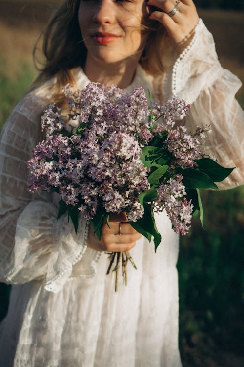 Woman in White Dress Holding Purple Flowers