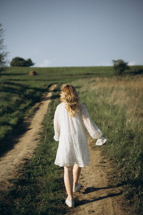 Back View of Blonde Person Walking on a Path in Grass Field 
