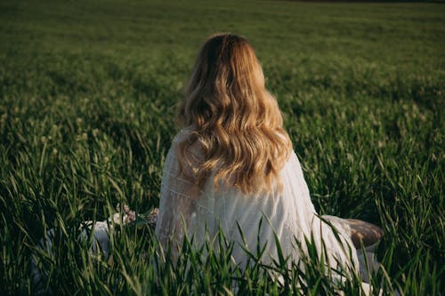 Free Woman in White Long Sleeve Dress Sitting on Green Grass Field Stock Photo
