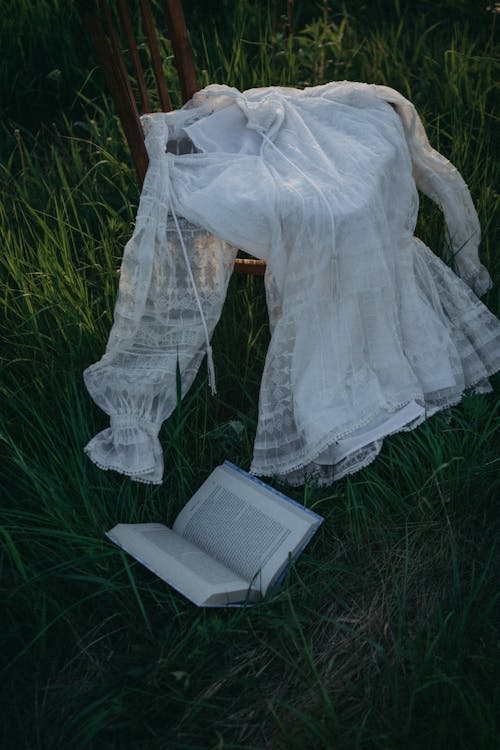 White Long Sleeves on a Chair Beside an Open Book
