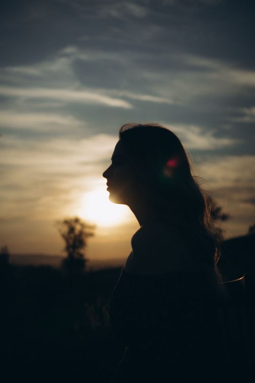 Free A woman's silhouette captured against a dramatic sunset, evoking tranquility and introspection. Stock Photo