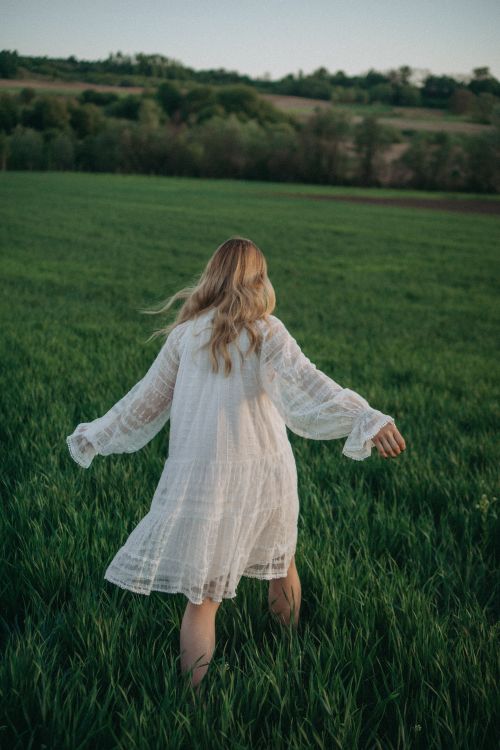 Free A woman in a flowing white dress runs through a lush green field, capturing a moment of freedom. Stock Photo