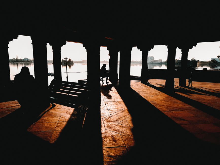 Atmospheric sunset scene with silhouettes and shadows at a lakeside pavilion.
