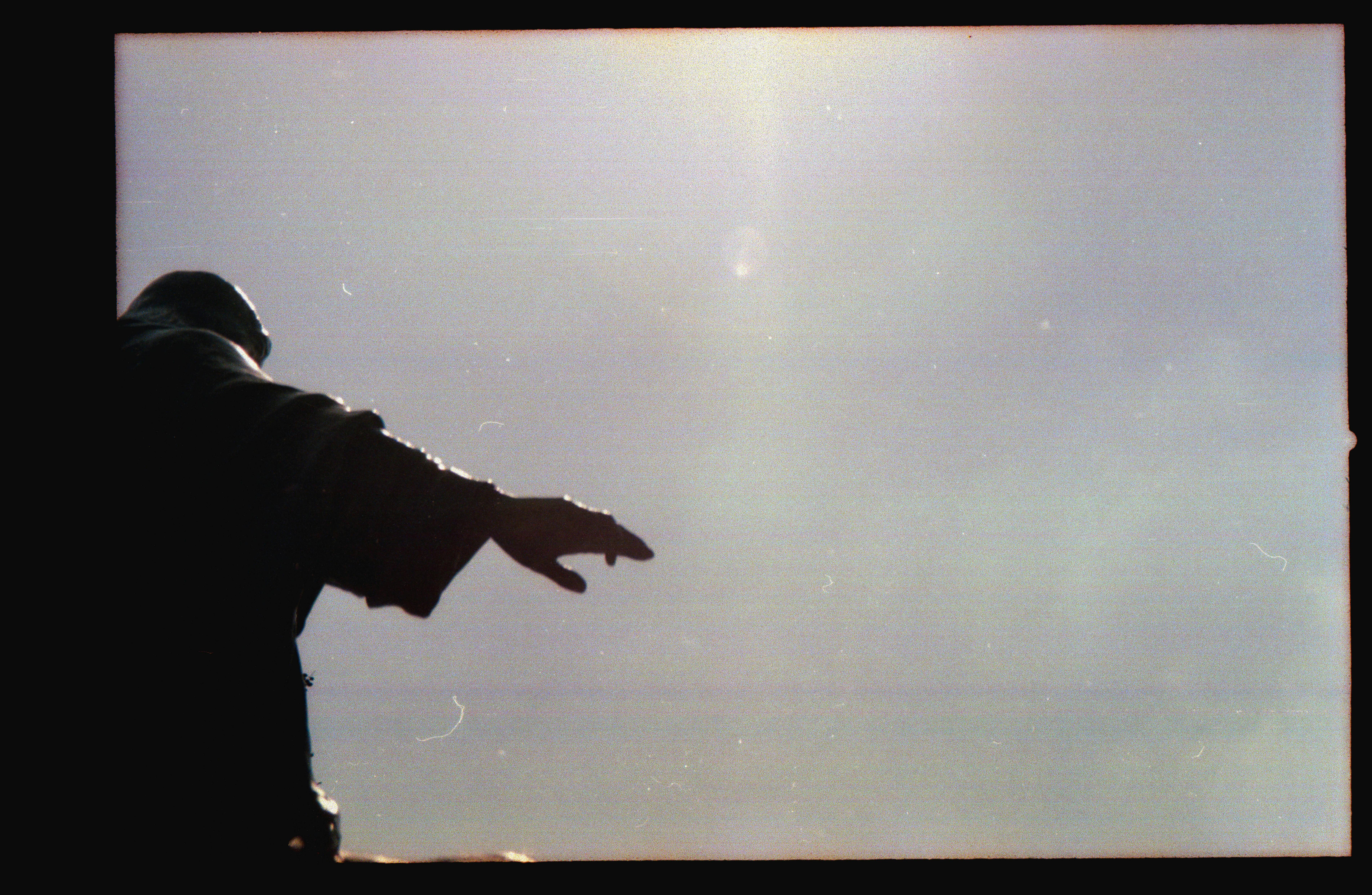 Silhouette of a hand reaching into a bright, clear sky, captured in a vintage style.