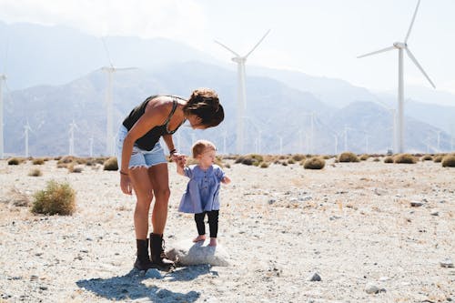 Woman Holding Her Child Walking Near Windmills