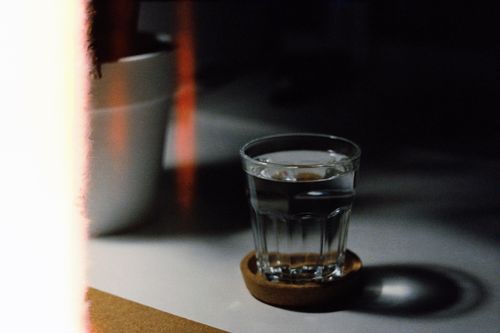 Free A moody, artistic photo of a glass of water on a coaster indoors, showcasing dramatic shadows and lighting. Stock Photo