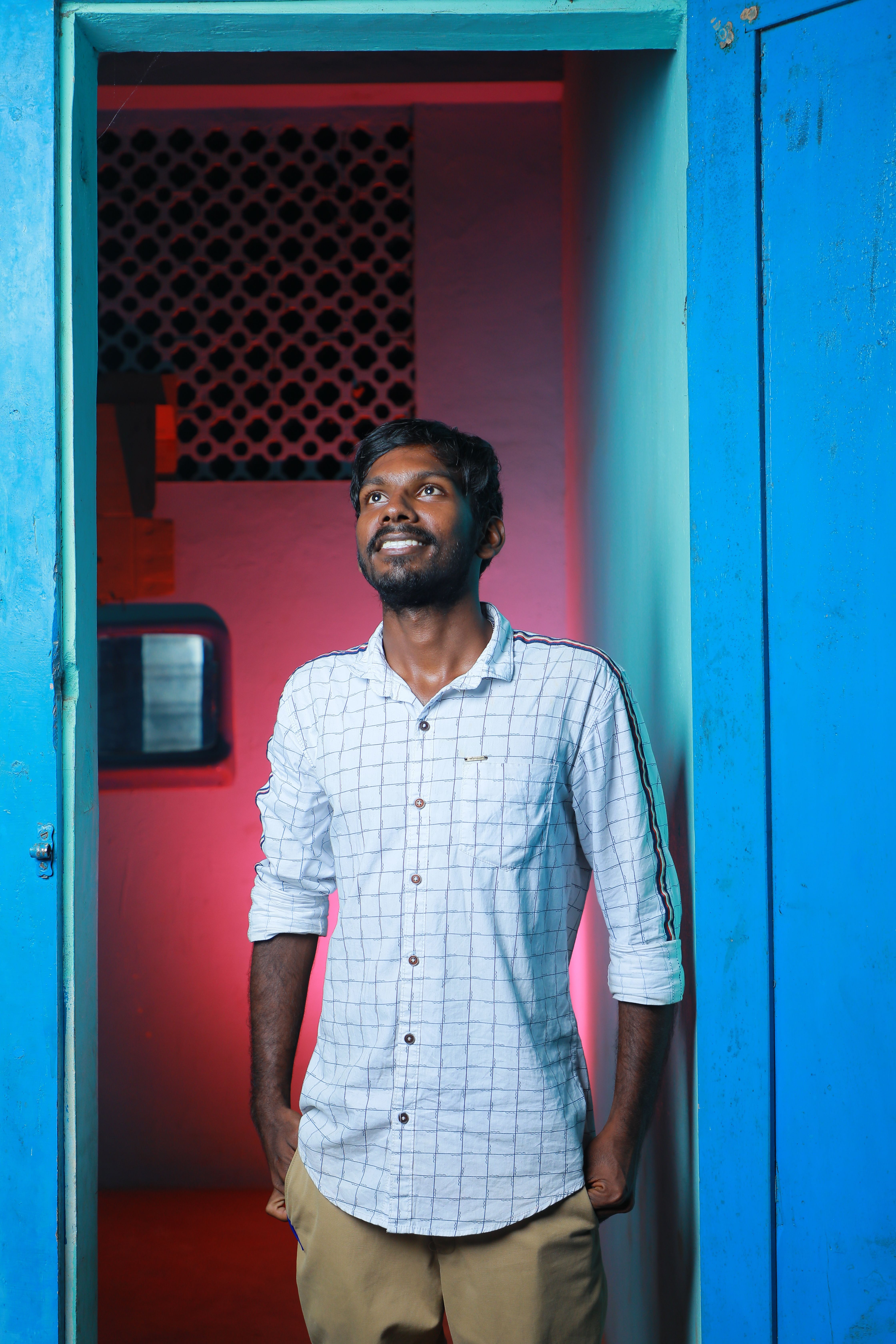 A man stands in a doorway with vibrant colors, looking upward with a thoughtful expression.