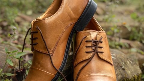 Stylish brown leather formal shoes placed on rocks in a natural setting.