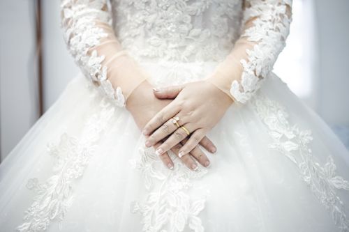 Free Detailed shot of a bride's hands showcasing rings on intricate lace wedding dress. Stock Photo