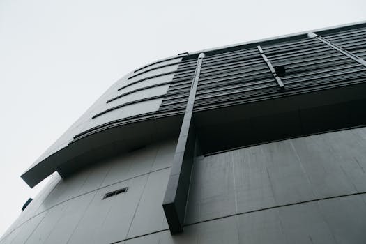Low angle view of a modern building with sleek architectural elements against a white sky.