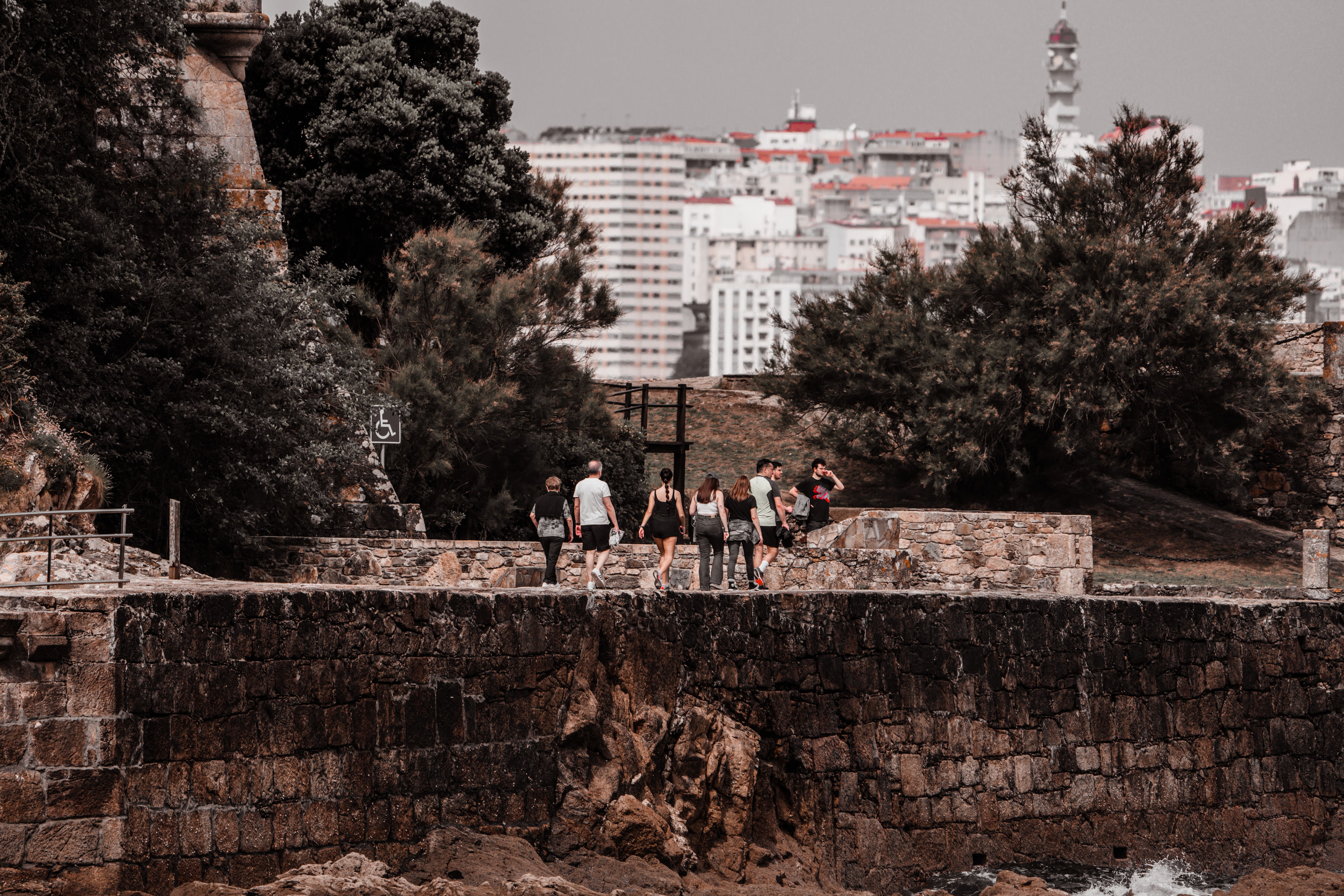 Tourists walking along the historic stone path at Porto de Santa Cruz with cityscape in background.