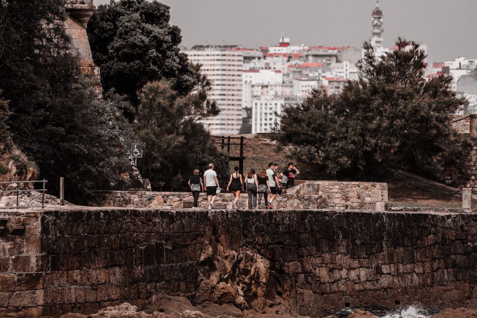 Turistas caminando por el histórico sendero de piedra en el Porto de Santa Cruz con la ciudad de fondo.