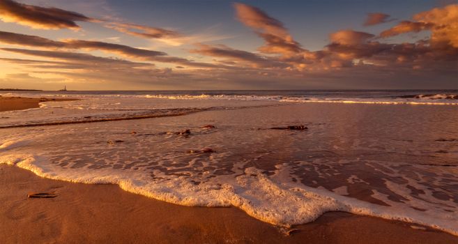 Peaceful beach scene during sunset with golden hues reflecting on the water.
