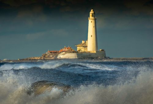 Free A lighthouse stands tall against stormy ocean waves under a dark sky. Stock Photo
