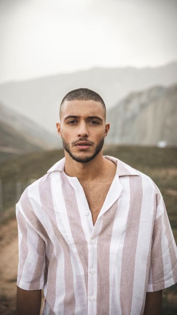 A confident man with stubble stands outdoors, exuding a serious look.