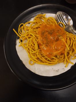 Close-up of a spaghetti dish with tomato sauce and herbs on a black plate, ready to eat.