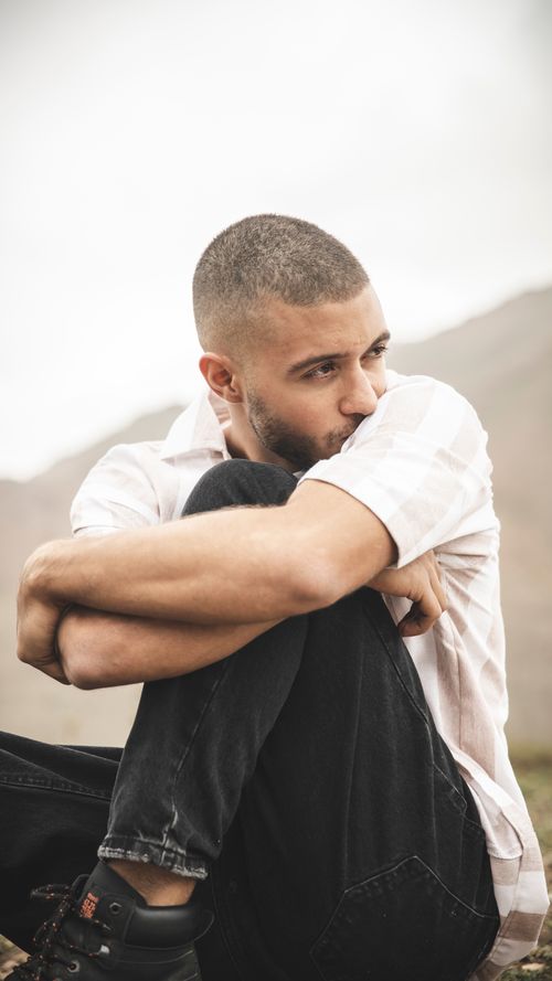 Free Thoughtful outdoor portrait of a young man seated, looking away, with a serious expression. Stock Photo